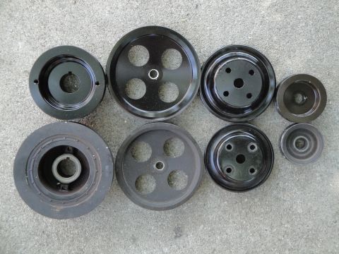 1995 Ford Taurus - Several engine pulleys are laid out on a gray concrete surface, showing different designs and hole patterns.
