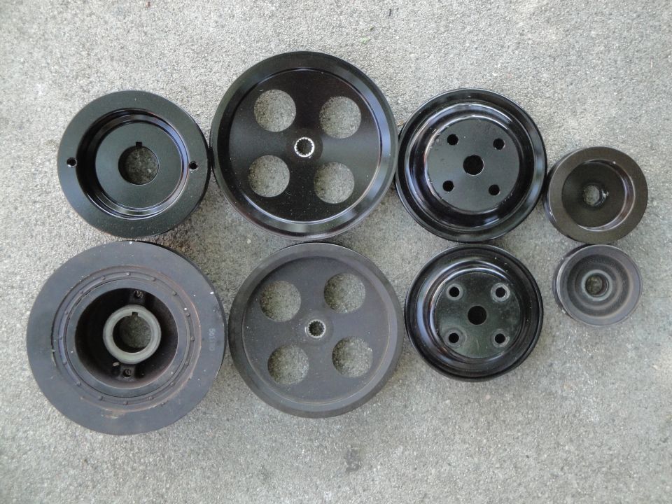 Collection of black metal automotive pulleys of various sizes and designs on a concrete surface