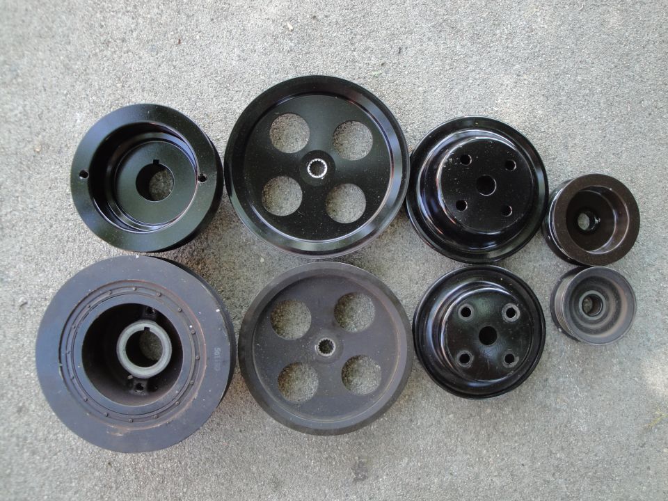 Several black metal car pulleys of different sizes laid out on a concrete surface