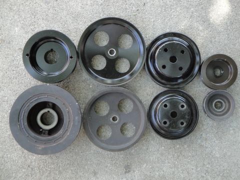 1995 Ford Taurus - A collection of automotive pulleys, including a large crankshaft pulley and several smaller accessory pulleys, are displayed on a gray conc…