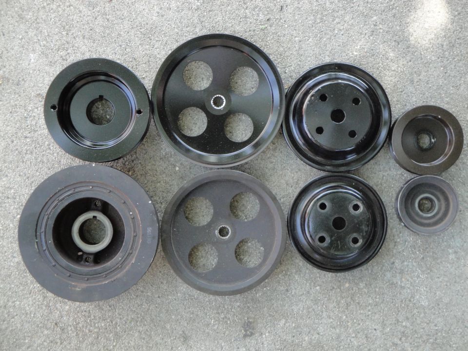 Assortment of black metal automotive pulleys of varying sizes and designs laid out on a concrete surface