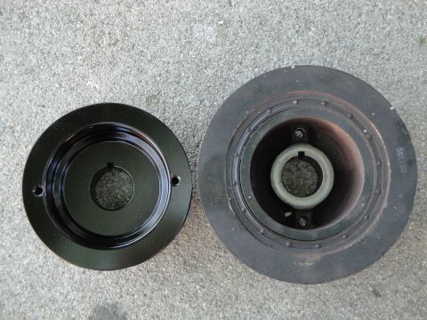 1995 Ford Taurus - Two crankshaft pulleys are shown side-by-side on a concrete surface. One is black and appears new, while the other is rusty and shows signs…