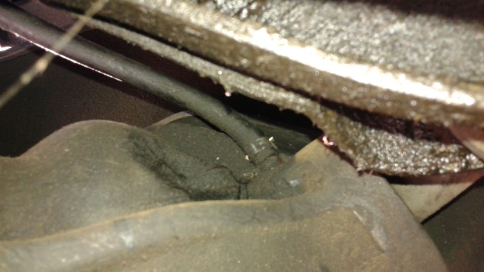 Close-up of greasy underbody mechanical parts with visible hoses and metal
