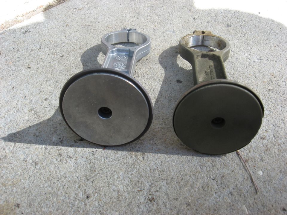 Two connecting rods, one new and one old, sit on concrete