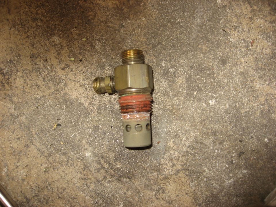 Close-up of an air compressor drain valve with brass fittings and a perforated metal end