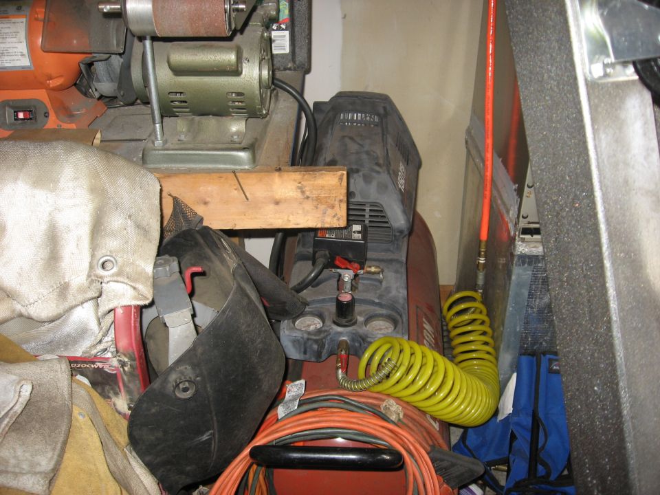 Red air compressor with black top, yellow coiled hose, and orange power cord