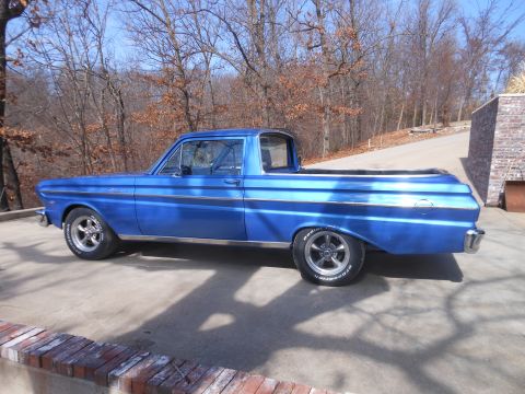 1965 Ford Ranchero - A blue 1965 Ford Ranchero pickup truck is parked on a concrete driveway with trees in the background.