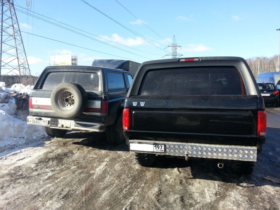Two black Ford Broncos parked on a dirt road with snow, one with a spare tire mounted on the rear door