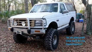 1992 Ford Bronco - A white 1992 Ford Bronco is shown with off-road modifications, parked in a wooded area.