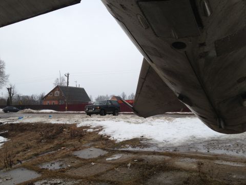 1987 Ford Bronco - A dark SUV is visible in the distance, parked near houses under a cloudy sky.