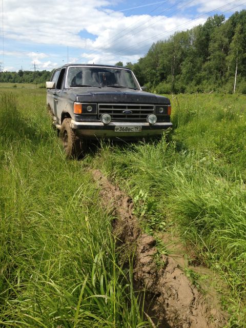 1987 Ford Bronco - 1987 Ford Bronco front view stuck in a muddy rut in a grassy field.