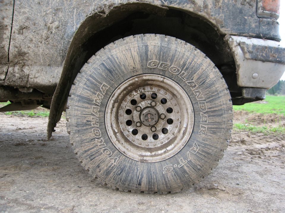 Close-up of a muddy Yokohama Geolandar A/T-S tire on a vehicle. The vehicle appears to be off-road