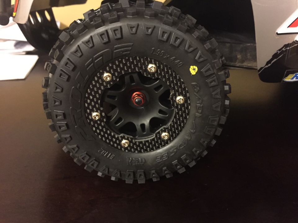 Close-up of a knobby RC car tire with a black and carbon fiber-look wheel. Some text is visible on the tire sidewall