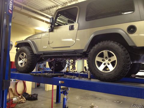 2005 Jeep Wrangler - A Jeep Wrangler is raised on a hydraulic lift in a garage, with tools laid out on the platform.