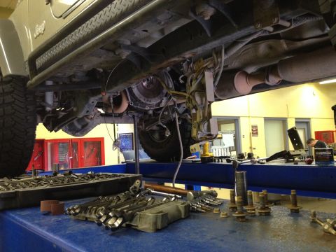 2005 Jeep Wrangler - Underside view of a Jeep on a lift, with tools and parts laid out on a workbench in the foreground.