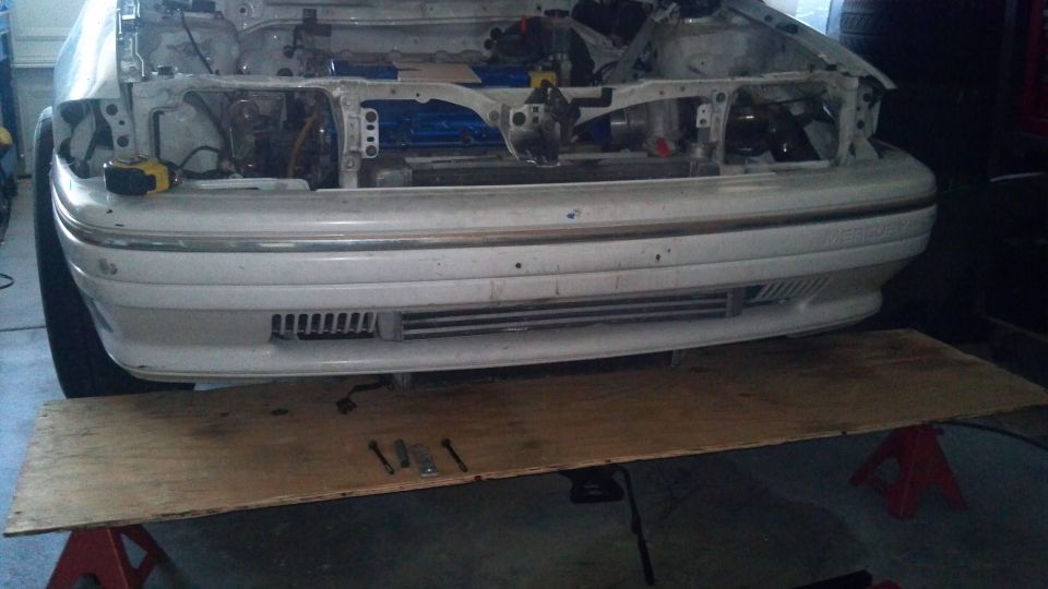 White car front bumper and grille with engine exposed, on jack stands