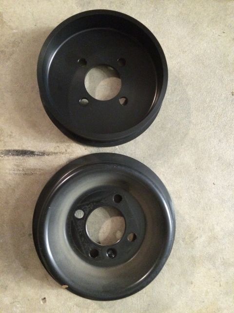 2003 Mercury Marauder - Two black pulleys, one appearing new and the other used, are displayed on a concrete floor.