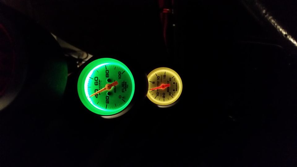 Two glowing gauges, one green and one yellow, in a dark car interior. The green gauge reads 'FUEL LEVEL'