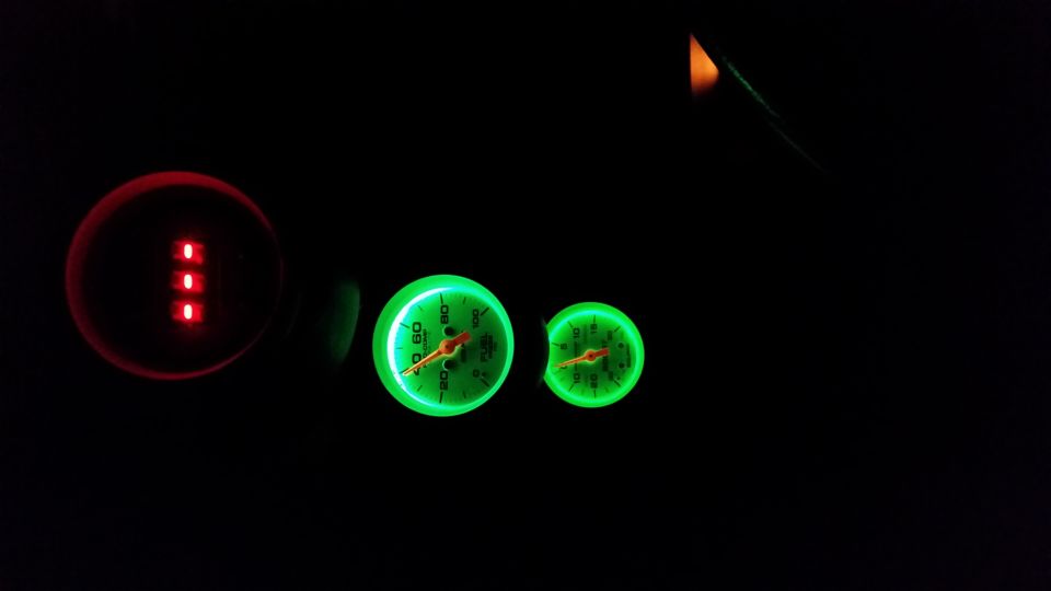 Dashboard gauges with red indicator lights and two green illuminated gauges, one larger than the other