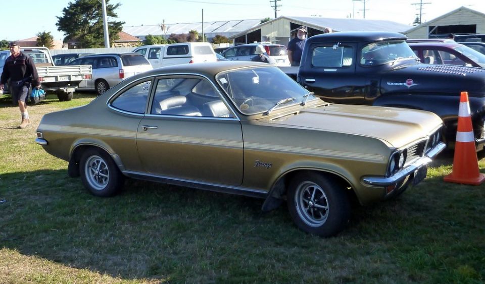 Gold coupe with a badge on the fender that reads 'Vauxhall' parked on grass