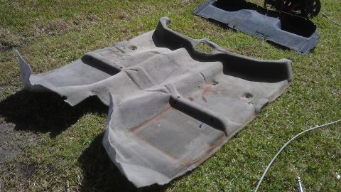 1994 Ford Bronco - Removed gray carpet from a vehicle's interior, lying on grass.