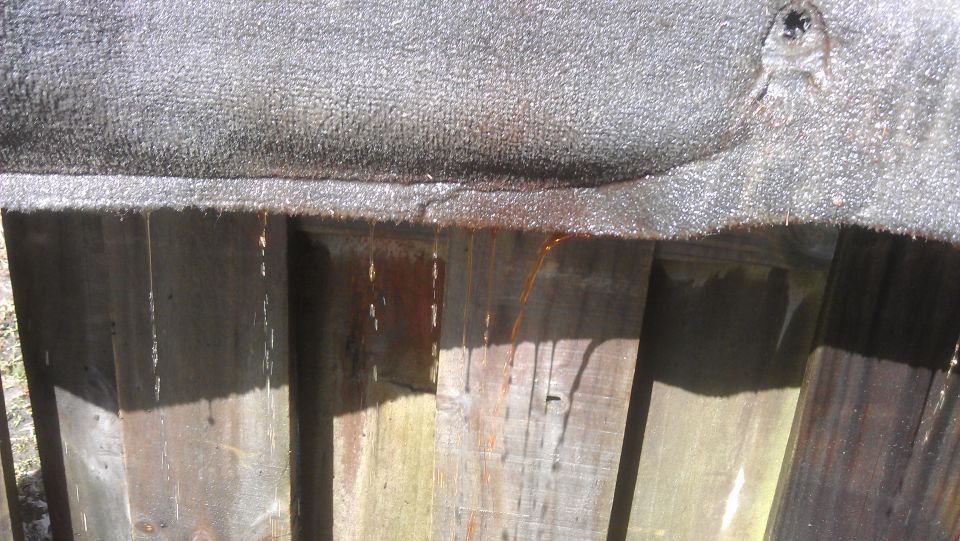 Water drips from a textured surface onto a wooden fence