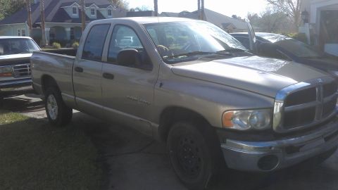 1994 Ford Bronco - A tan Dodge Ram pickup truck is parked in a driveway next to another vehicle. The truck's grille and headlights are visible.