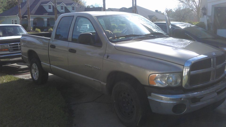Tan Dodge Ram pickup truck, 3/4 front view. Another vehicle is partially visible on the left