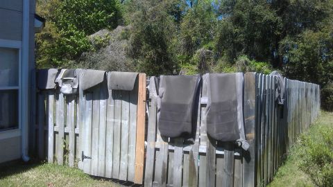 1994 Ford Bronco - Various car seat covers and interior parts are hung on a weathered wooden fence to dry or air out.