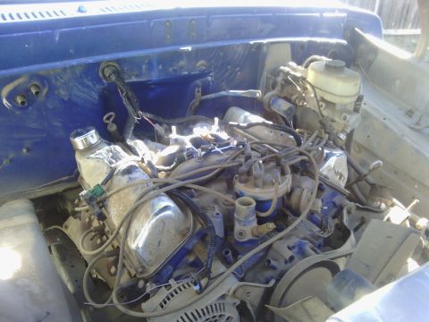 1978 Ford Bronco - The engine bay of a blue vehicle shows various mechanical parts and wiring harnesses.