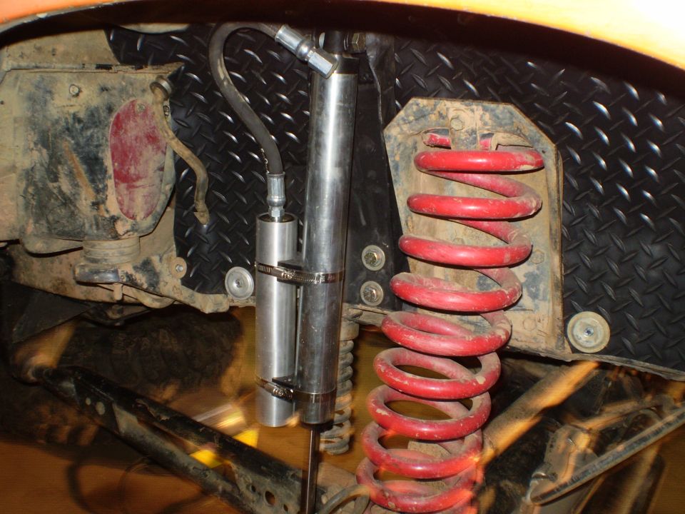 Suspension components including a red coil spring and a silver shock absorber with a hydraulic line