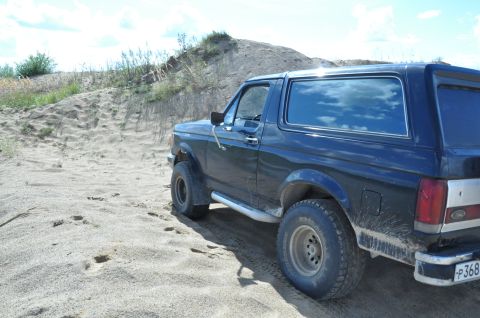 1987 Ford Bronco - 1987 Ford Bronco navigating sandy terrain under a partly cloudy sky.