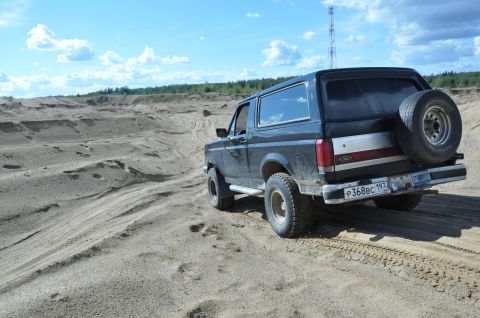 1987 Ford Bronco - 1987 Ford Bronco navigates sandy terrain, spare tire visible on the rear.