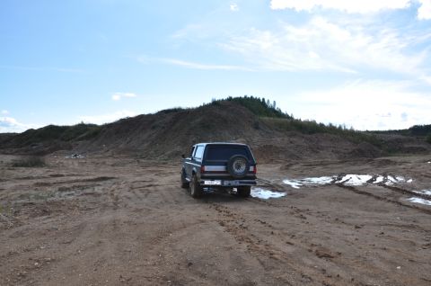1987 Ford Bronco - A Ford Bronco sits in a muddy, off-road area under a partly cloudy sky.