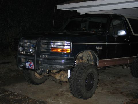 1995 Ford Bronco - 1995 Ford Bronco modified with a bull bar and oversized tires, parked under a carport at night.