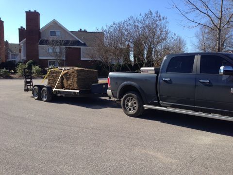 1989 Ford Bronco - Pickup truck hauls sod on a trailer, with apartment buildings in the background.