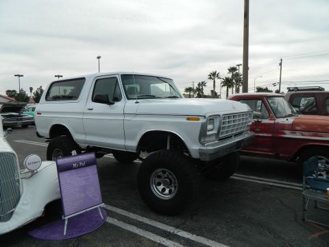 1979 Ford Bronco - A white SUV with a lifted suspension and large off-road tires is displayed at an outdoor event next to other vehicles.