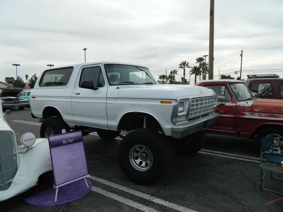 White lifted SUV with large tires parked next to a red truck. A sign says 'My Pal'