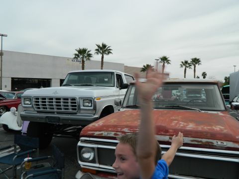 1979 Ford Bronco - A lifted white 1979 Ford Bronco is parked next to a rusty red pickup truck, with a child waving in the foreground.