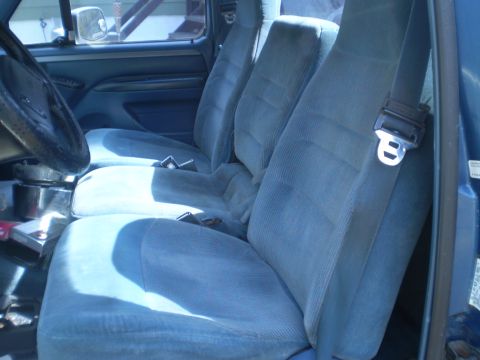 1979 Ford Bronco - The interior of a blue vehicle shows three front seats and seatbelts.