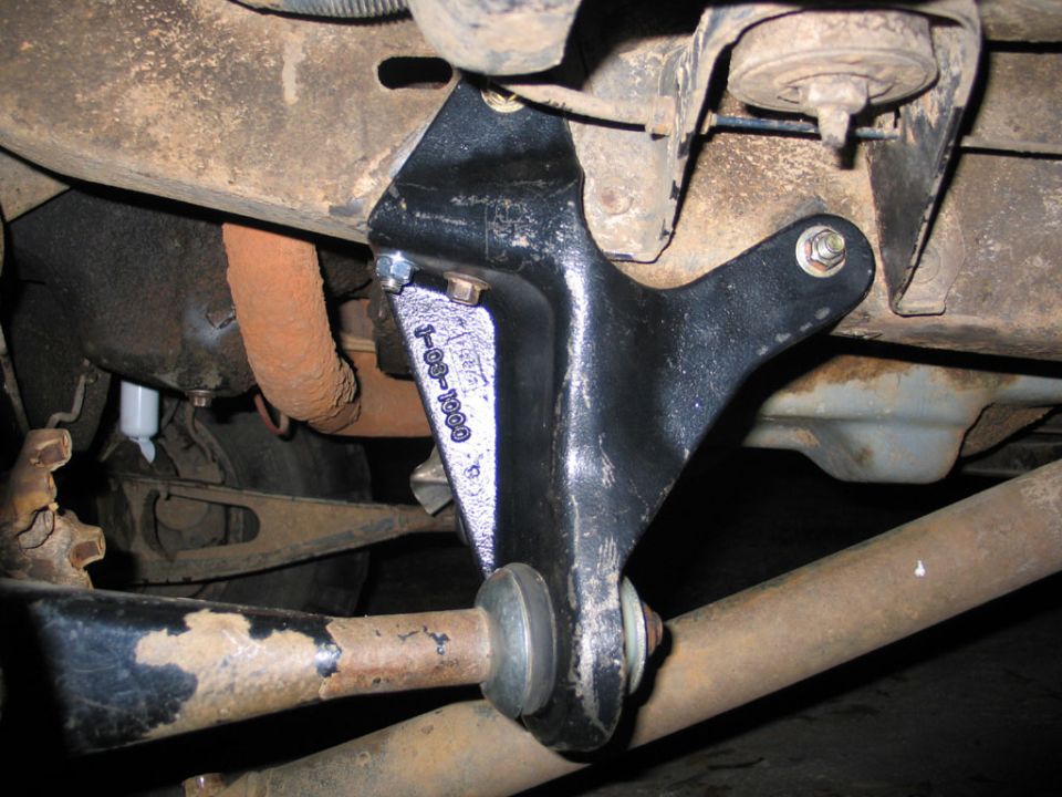 Black radius arm drop bracket bolted to a rusty truck frame, underbody view