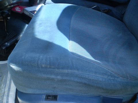 1979 Ford Bronco - The interior of a vehicle shows a blue fabric seat with a shadow cast across it.