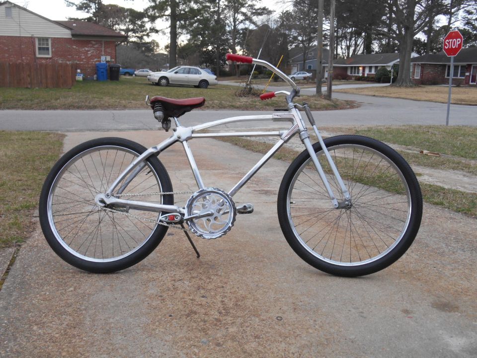 Chrome cruiser bicycle with red handlebars and seat, parked on a sidewalk