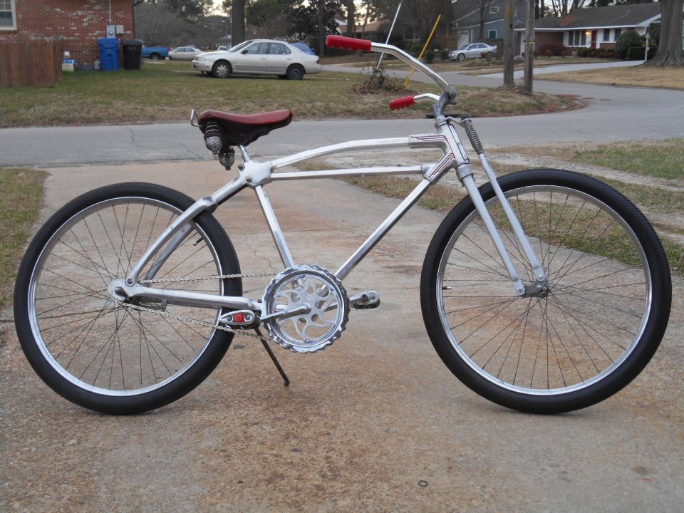 Chrome cruiser bicycle with red handlebars and seat, parked on a driveway
