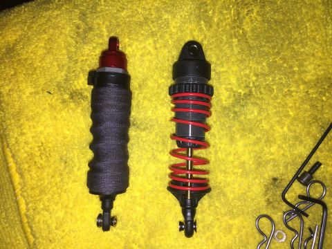 2014 Dodge 1500 - Comparison of two shock absorbers, one a textured sleeve and the other with prominent red springs, laid out on a yellow cloth.