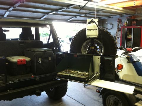2005 Jeep Wrangler - The rear interior of a Jeep Wrangler is equipped with camping gear, including coolers and a portable stove, next to a snowmobile.
