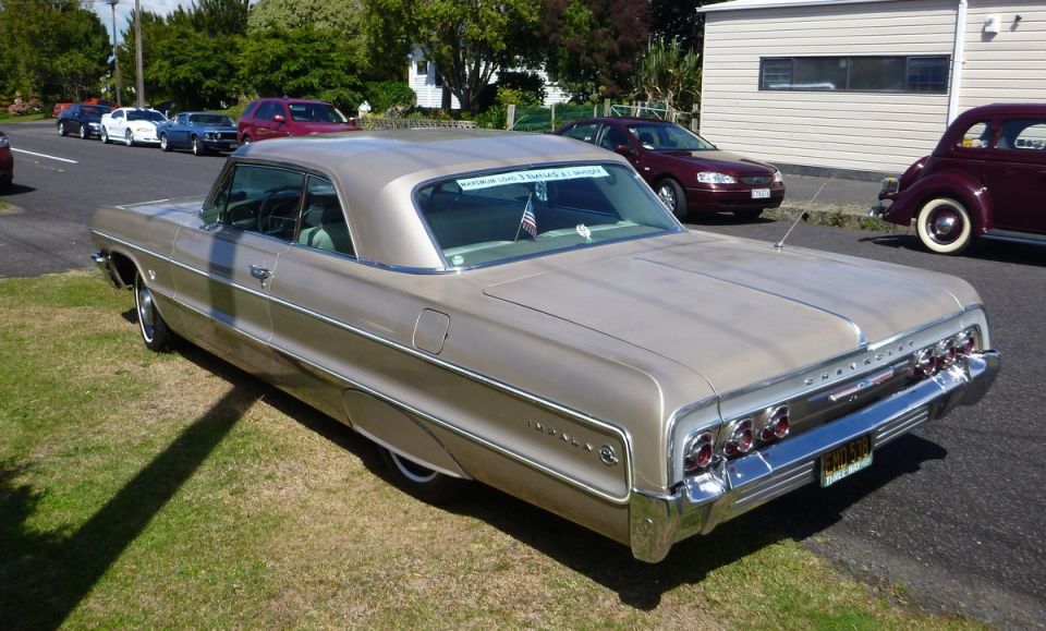 Champagne 1964 Chevrolet Impala coupe rear view, chrome bumper, quad taillights, on grass next to road
