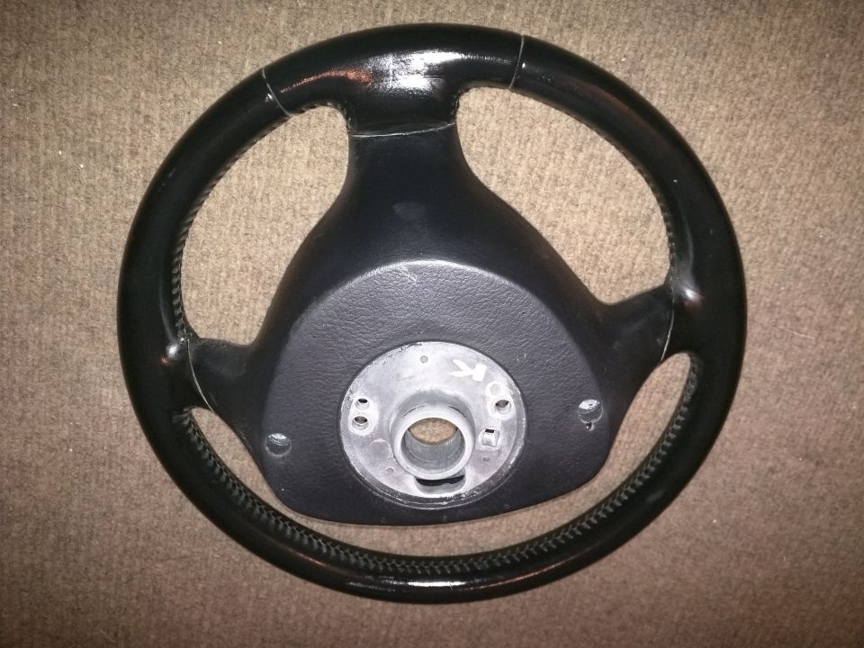 Black steering wheel with a silver hub, resting on a carpeted surface