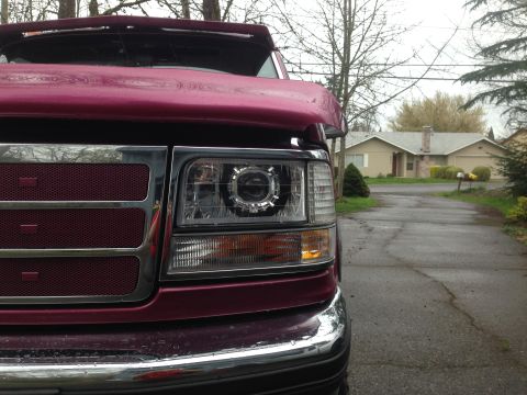 1992 Ford F-150 - Close-up of a Ford F-150's front end, highlighting its custom headlights and grille, with a suburban street visible behind it.