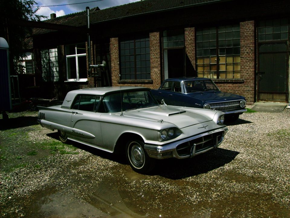 1959 Ford Thunderbird parked next to a blue car in front of a brick building